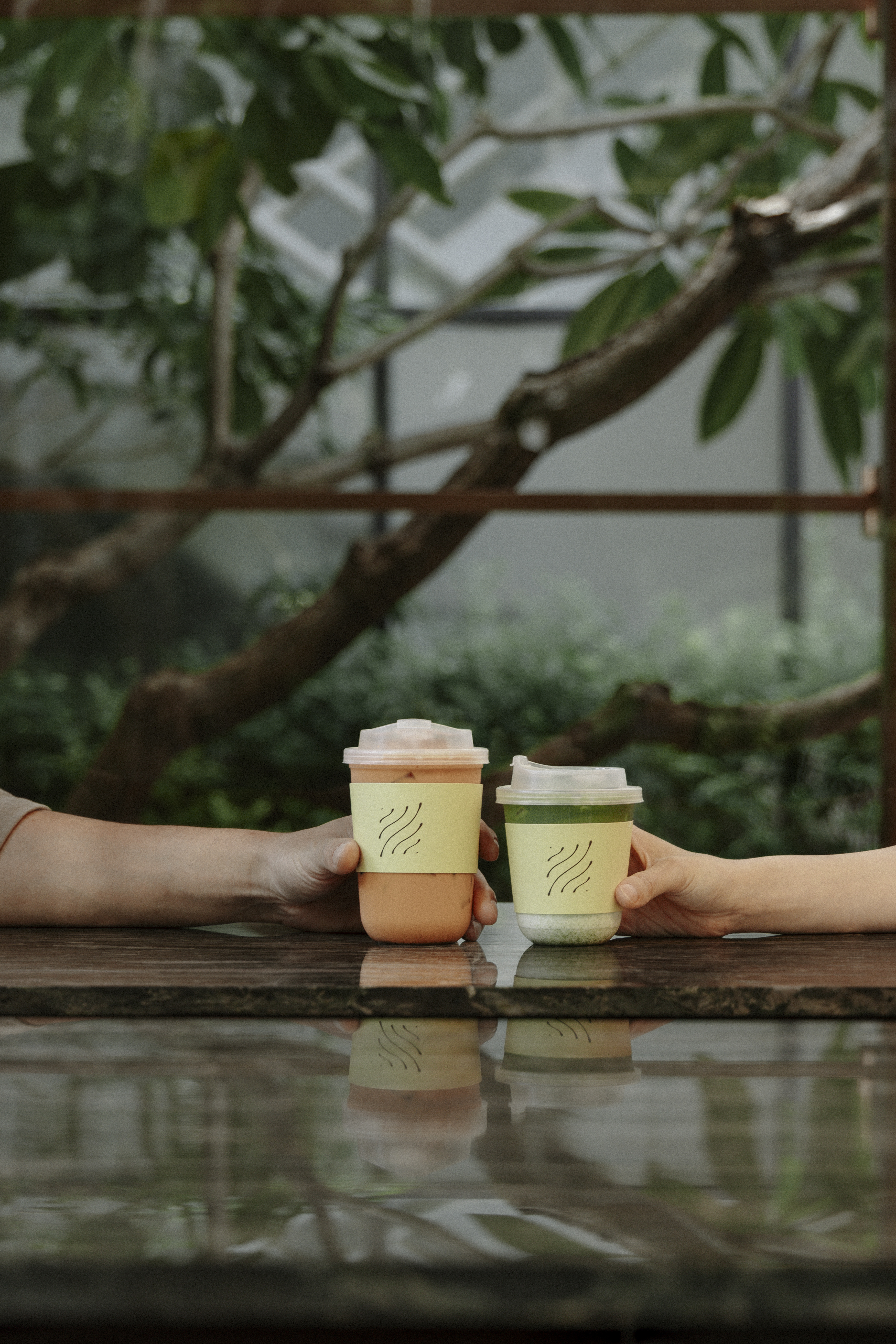 Two hands toasting LOM cups with trees in background