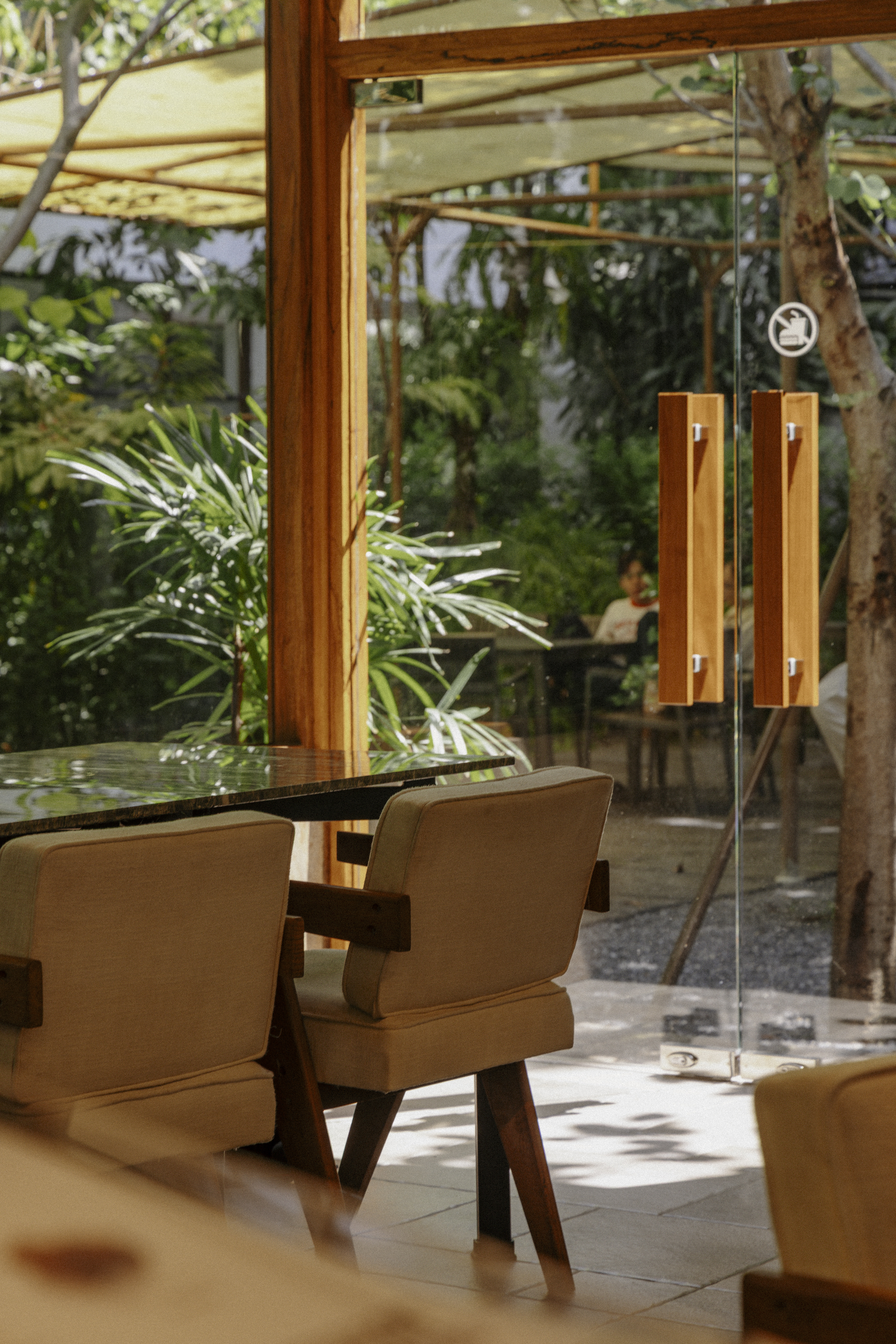 Café LOM — wooden chairs and green marble tables with garden through glass